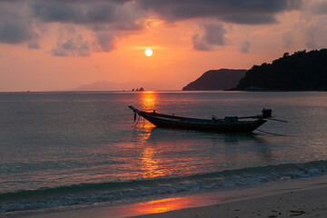 Tropical beach and a wooden fishing boat at sunset.