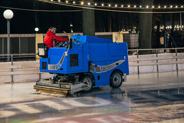 A stadium worker cleans an ice rink on a blue modern ice cleaning machine. - Powered by Adobe