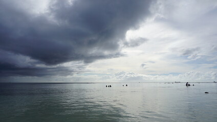 Swimming people under stormy sky with dark clouds before rain at a quiet beach in Saipan 