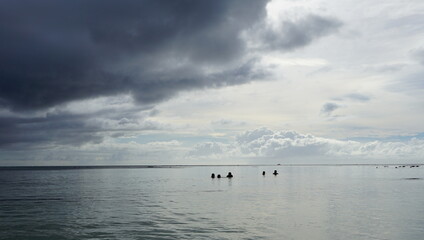 Fototapeta na wymiar Swimming people under stormy sky with dark clouds before rain at a quiet beach in Saipan 