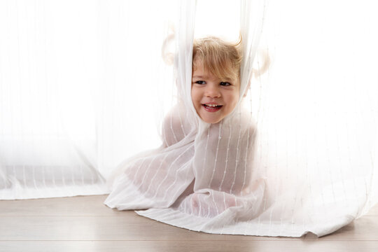 Cute happy face of little girl peeking through curtains at home