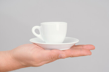A classic coffee mug with a saucer stands on an open man's palm