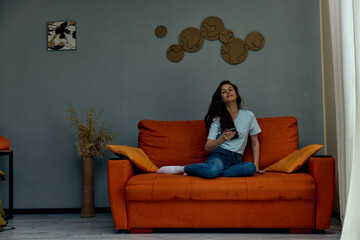 smiling woman chatting on the orange couch with a smartphone technologies