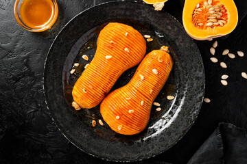 Baked pumpkin or butternut squash with honey served with roasted pine nuts. Black background. Top...