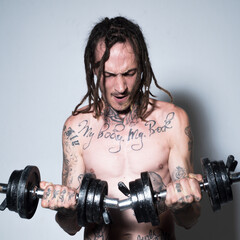 Portrait of funny hipster with dumbbells. Shirtless man man with muscles torso in studio.