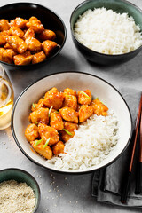 Crispy Honey Sesame Chicken garnished with basmati rice, korean style food. Light gray stone background.