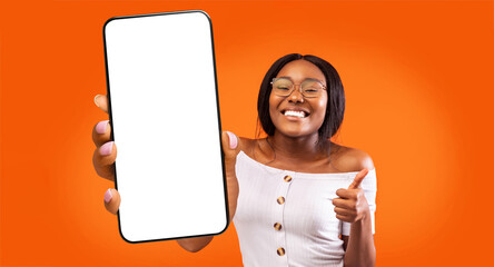 Great app. Overjoyed black lady holding big smartphone with white blank screen and showing thumb...