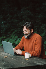 Happy free adult man work outdoors on a table with nature in background - concept of digital nomad...
