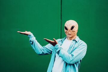 Portrait of ufo alien extraterrestrial mask with denim casual clothing like a human and green wall...