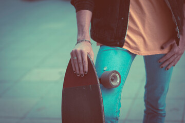 Close up of boy hand with black nails holding skate board with city asphalt street in background -...