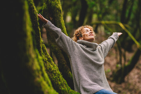 Overjoyed happy woman enjoying the green beautiful nature woods forest around her - concept of female people and healthy natural lifestyle - happiness emotion and adult lady opening arms close eyes