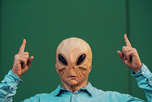 Portrait of ufo alien extraterrestrial mask with denim casual clothing like a human and green wall in background for copyspace text
