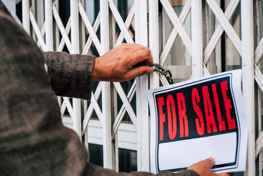 Close up of professional business man putting for sale box panel on the closed door of a store  concept of selling and buying properties and economy crisis - seller or owner close his activity
