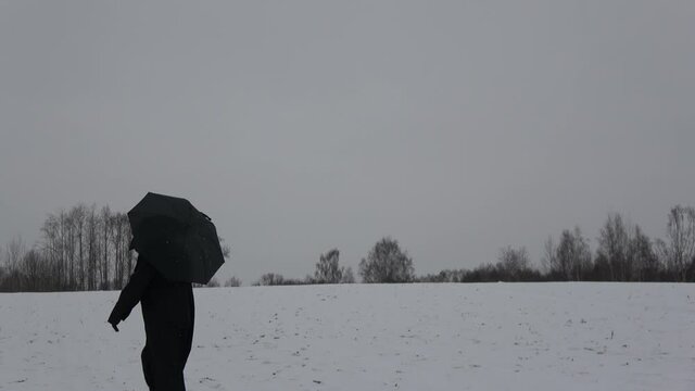 Plaque doctor in black bird beak mask with umbrella goes through a snowy field.   Image of all pandemics