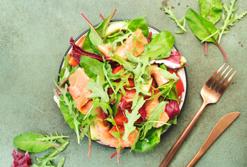 Fresh salmon salad with avocado, beet leaves, radicchio, tomatoes, lemon and olive oil dressing for keto and low carb diet. Rusty green background, top view, copy space