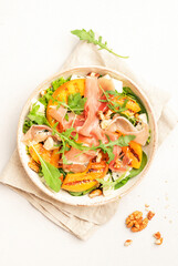 Salad bowl with grilled peach, jamon, feta cheese, nuts and arugula on white table background, top view, copy space