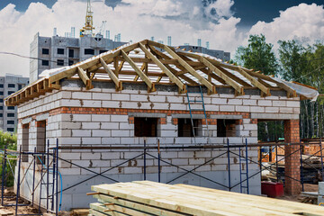 Building site of a house under construction. Unfinished house walls made from white aerated autoclaved concrete blocks. Wooden truss system.