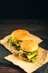Tasty hamburgers on wooden board on dark background.