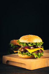 Tasty hamburgers on wooden board on dark background.