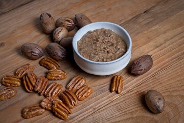 Organic pecan nut butter in bowl with raw pecans on a wooden table