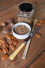 Organic pecan butter in bowl and glass jar with raw pecans on a wooden table