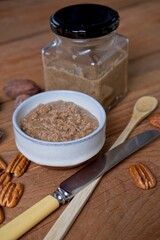 Organic pecan nut butter in bowl and glass jar with raw pecans on a wooden table