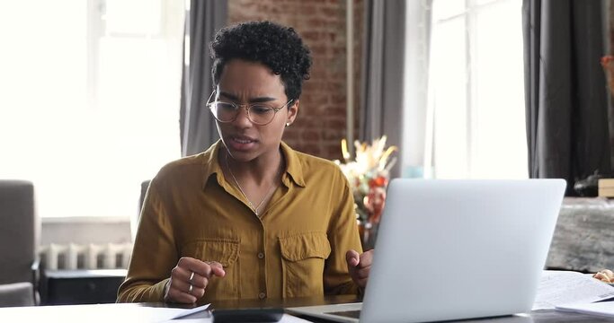 Bad-tempered African woman sit at desk do accounting job or manage personal finances, reviewing bills feels upset due huge taxes, sum need to pay, experiences lack of money, crisis, bankruptcy concept