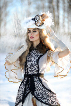 A young beautiful blonde in a historical image stands on the snow in a winter forest in a hat made of feathers. Retro style. Art portrait