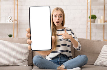 Surprised woman showing phone blank screen to camera and pointing finger on it, recommending cool...