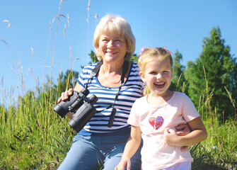 Little girl with her grandmother looking through binoculars outdoor