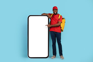 Order Online. Black Delivery Guy With Thermal Backpack Pointing At Blank Smartphone