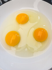 Three bright yellow raw chicken eggs in a white bowl.