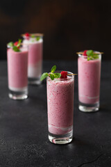 Raspberry milkshake or smoothie in a glasses decorated with mint and raspberries on a black background.