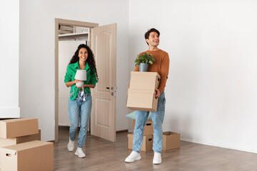 Happy couple holding cardboard boxes, walking in new house