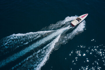 White boat on the water top view. White boat with people on blue water in the rays of the sun aerial view. Boat in motion top view.