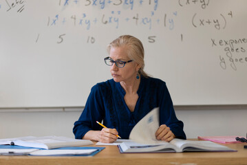 Portrait of high school math teacher sitting at desk working on assignments for students.