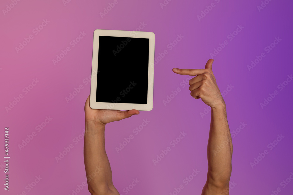 Poster Cropped view of millennial man pointing at tablet computer with empty black screen in neon light, mockup