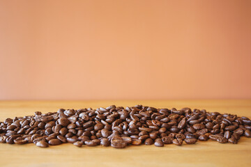 Heap of roasted coffee beans on wood desk with brown background 