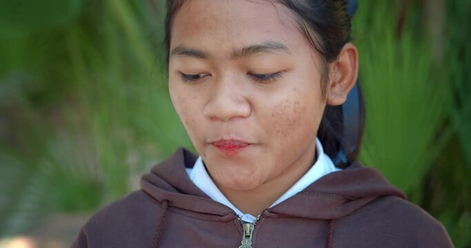 A teenage Asian female student who has acne on the face, eating a delicious red and green ice cream stick.