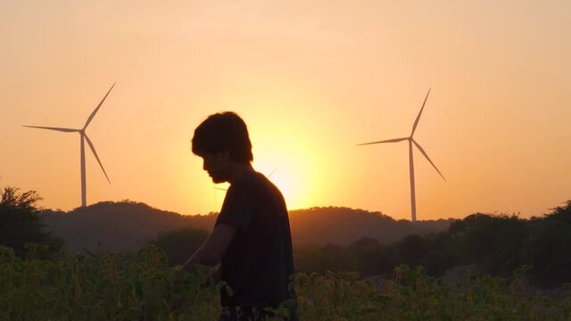 Silhouette shot of a young Indian man walking in the fields in front of the windmill above the hills at Wankaner in Gujarat, India. Selective focus on the windmills on hills in the background.