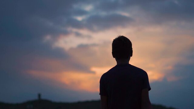 Silhouette shot of an Indian kid walking in front of the clouds during the sunset. Kid walking towards the light rays during the sunset. Light rays signifies new beginning for the kid. Hope concept. 