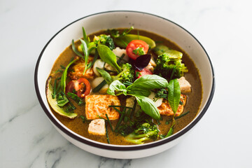 vegan thai green curry with fried silken tofu broccoli and snow peas topped with freshly picked herbs from the garden, healthy plant-based food
