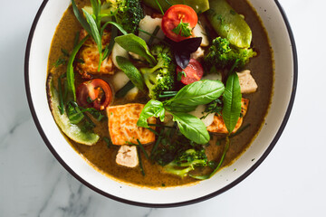 vegan thai green curry with fried silken tofu broccoli and snow peas topped with freshly picked herbs from the garden, healthy plant-based food