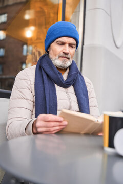 Senior man in a warm clothes sitting with a book at the cafe terrace
