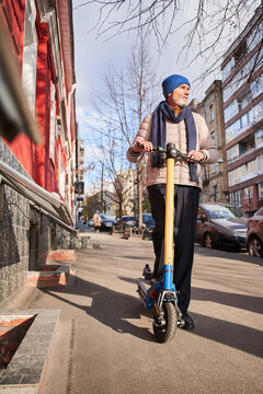 Mature man wearing warm clothes riding on electric scooter on the street