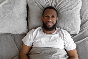 Black man lying in bed and thinking, top view