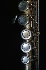 Closeup detail of keys on central part of transverse flute (this part is also called middle joint) with visible signs of heavy use and corrosion of silver coating, dark background.  © zayacsk