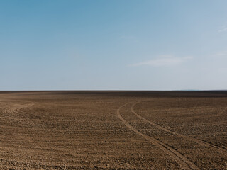 Fototapeta na wymiar brown field under blue sky with wheel tracks on it