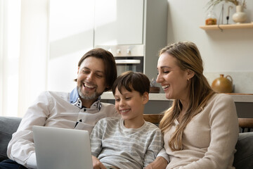 Happy millennial 40s family couple and gen Z teenage kid resting on couch together, watching online movie, series, media on computer, using virtual app on laptop for shopping on Internet from home