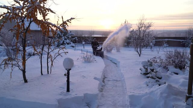 Kaluga region, Russia -January 06 -2022: An elderly man cleans snow with a snowplow in the garden of a country house in winter.